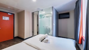 Hotelkamer met een bed, een douche en een televisie die aan de muur hangt, plus een rode deur.