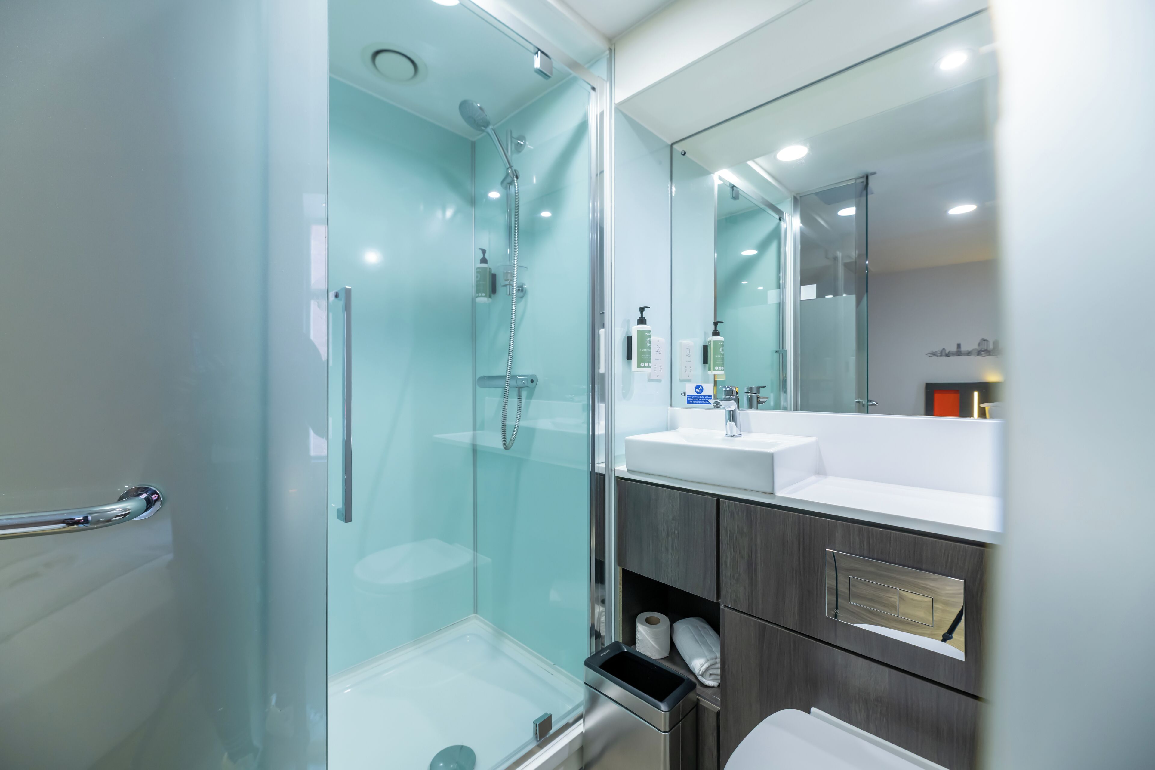 Un bagno moderno con cabina doccia in vetro, lavandino bianco e uno specchio grande.