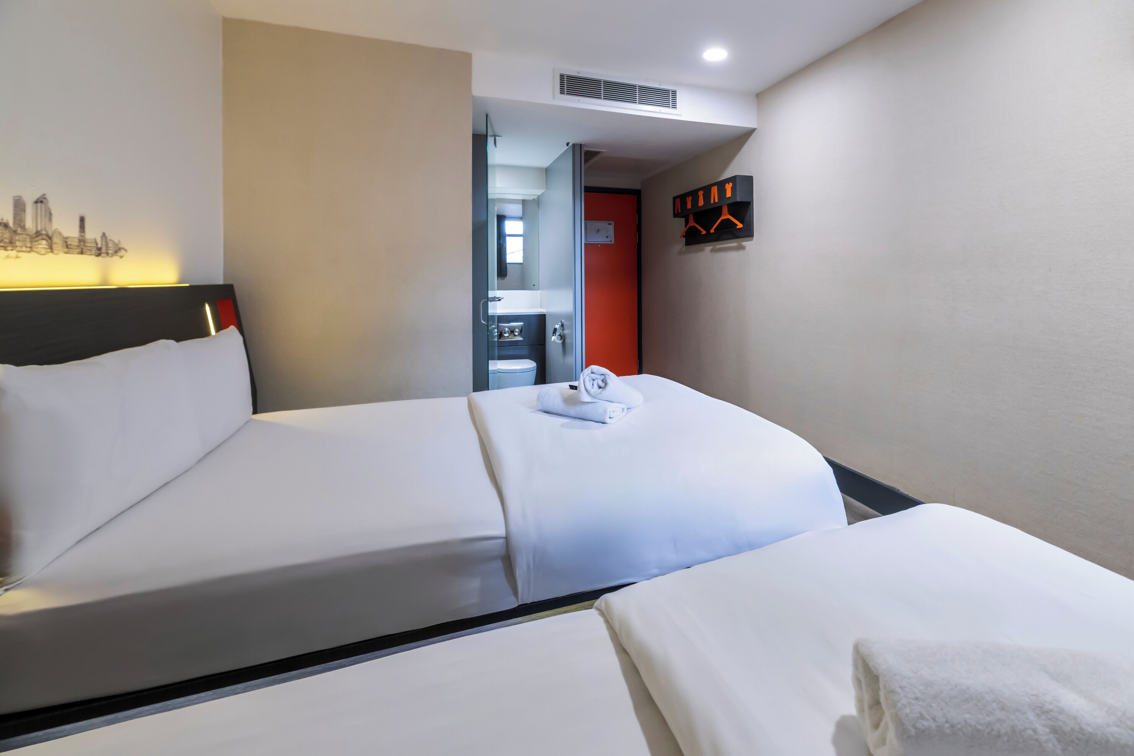 Habitación de hotel con dos camas, una obra de arte urbana, una puerta roja y una toalla sobre una cama.