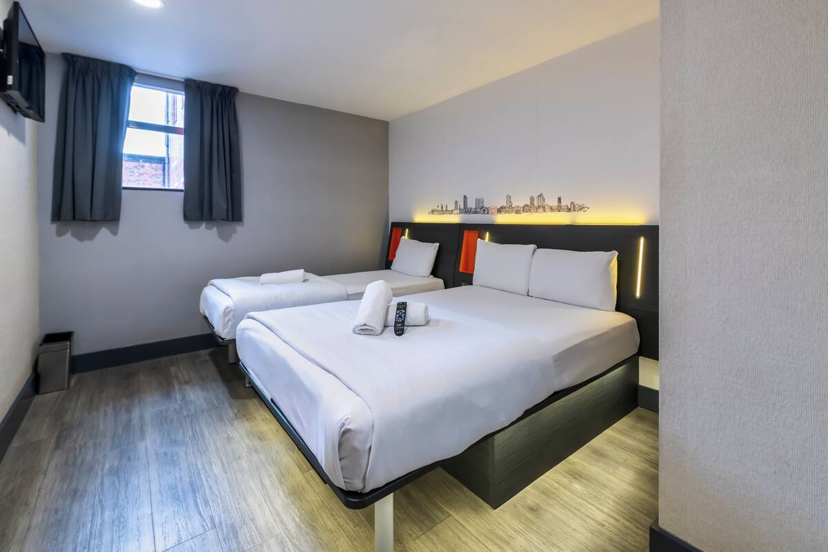 A hotel room with two beds, a cityscape wall art, and a window with curtains.