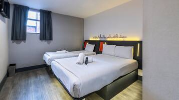 A hotel room with two beds, a cityscape wall art, and a window with curtains.