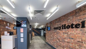Een receptiegedeelte met een bakstenen muur, een receptiebalie met de tekst 'WELKOM' en een bord waarop 'easyHotel' staat.