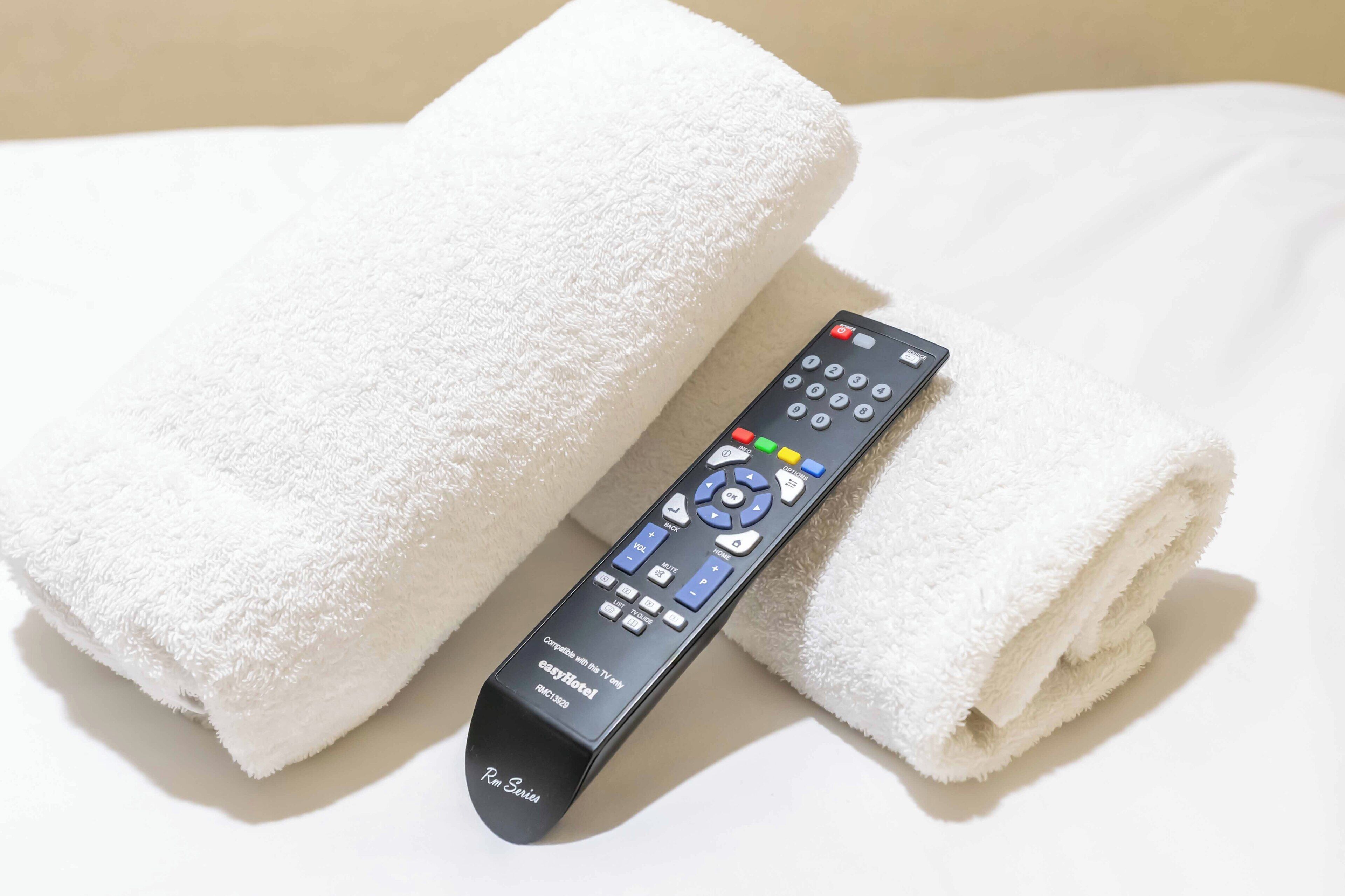 Un telecomando e un asciugamano bianco piegato su un letto.
