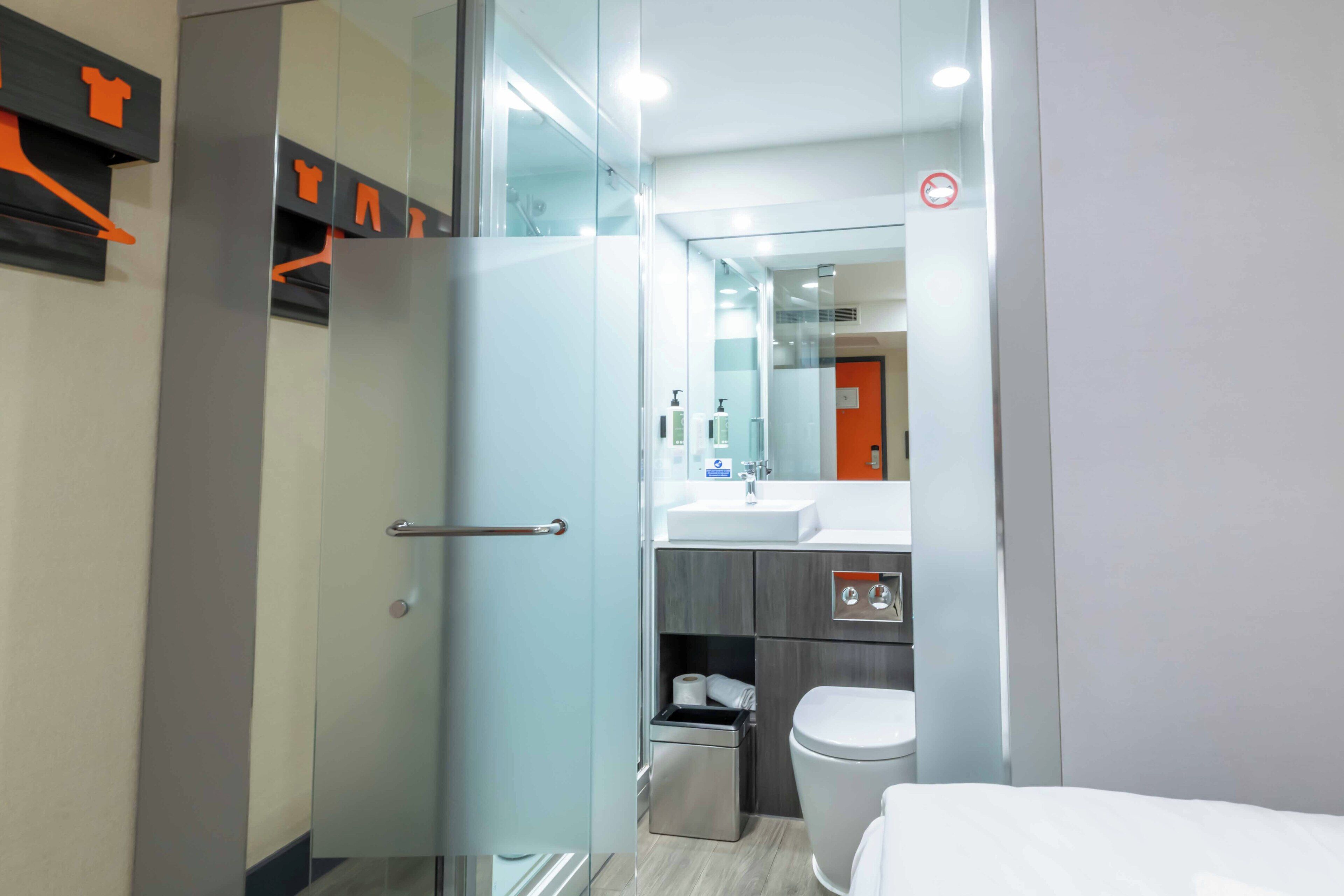 Une salle de bain moderne avec une douche à parois de verre, des toilettes blanches et un lavabo surmonté d’un miroir.