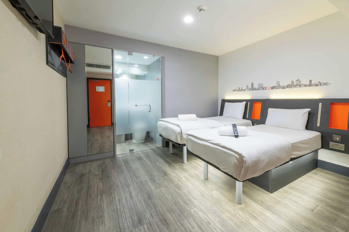 A modern hotel room with two beds, a cityscape wall art, and a glass door leading to a bathroom.