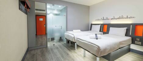 A modern hotel room with two beds, a cityscape wall art, and a glass door leading to a bathroom.