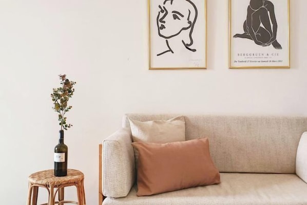 A room with a beige sofa, a small round wicker stool with a bottle of wine, and two framed artworks on the wall. - The51Hometel (Chiangmai)