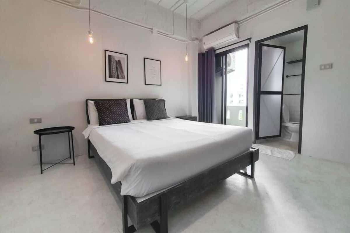 Une chambre à coucher moderne, avec un lit, une petite table de chevet et une porte donnant sur une salle de bain.