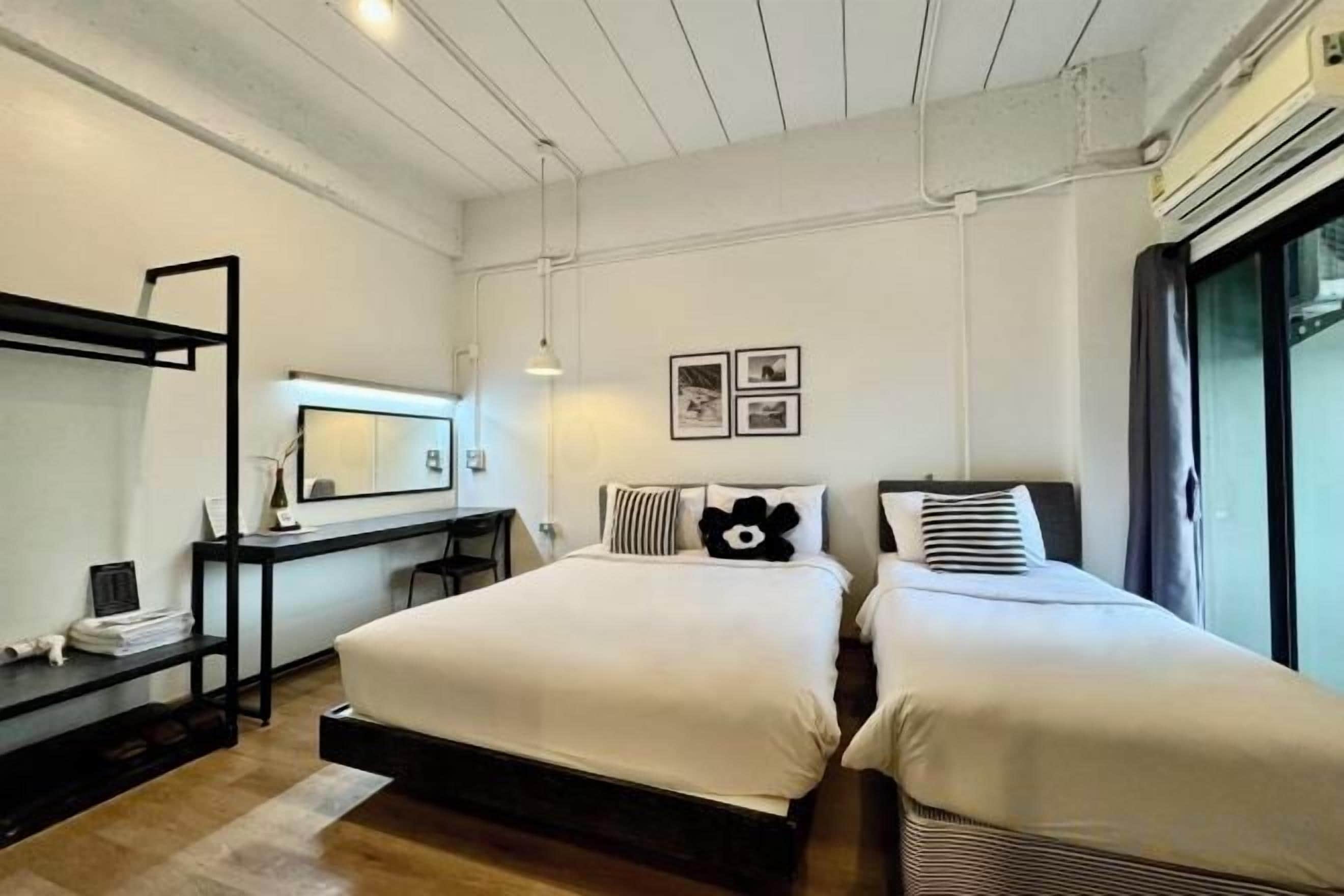 A bedroom with two beds, a desk, a chair, and a large window.