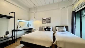 A bedroom with two beds, a desk, a chair, and a large window.