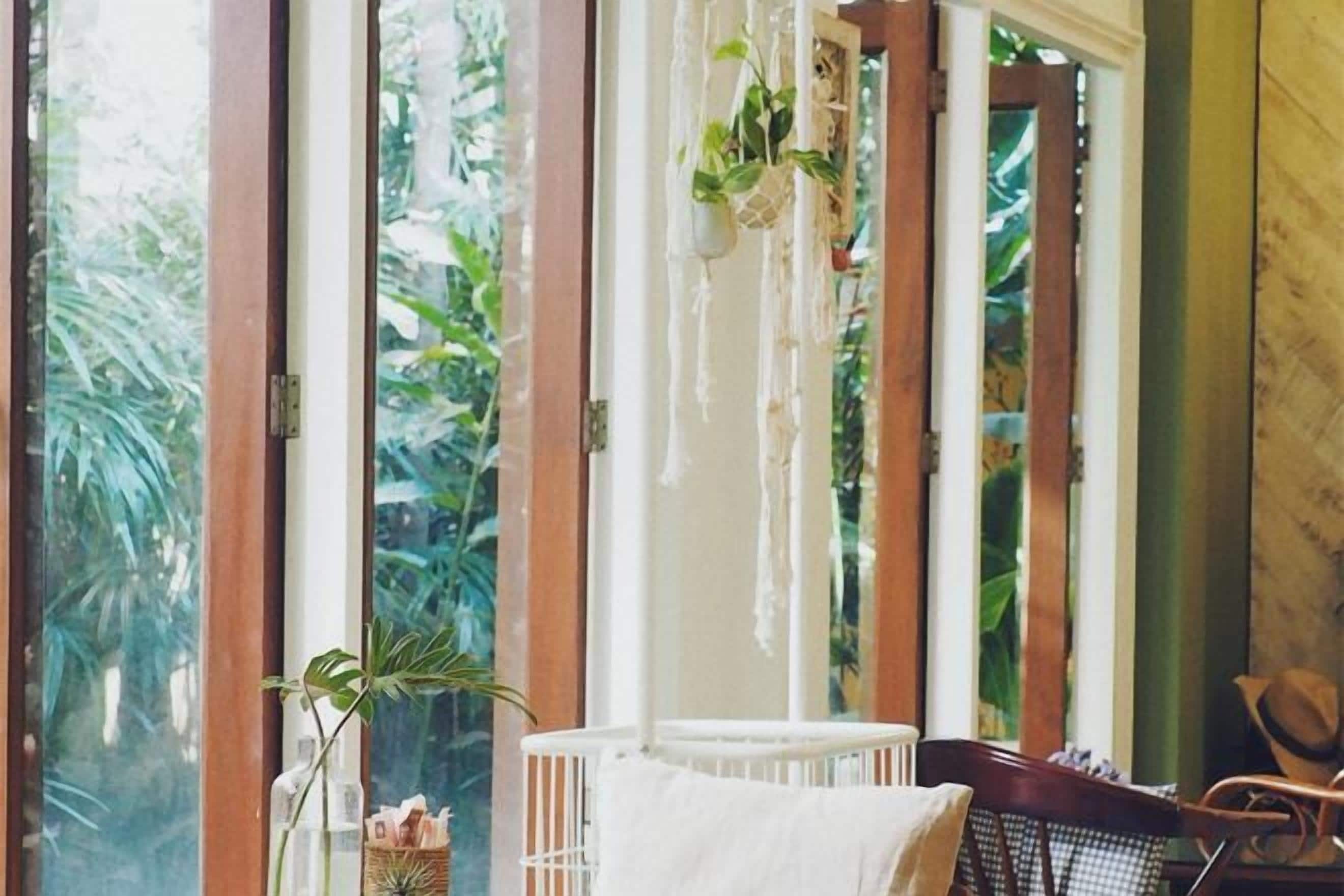 Une chambre avec un berceau, un fauteuil et une vue sur la verdure grâce à de grandes fenêtres.