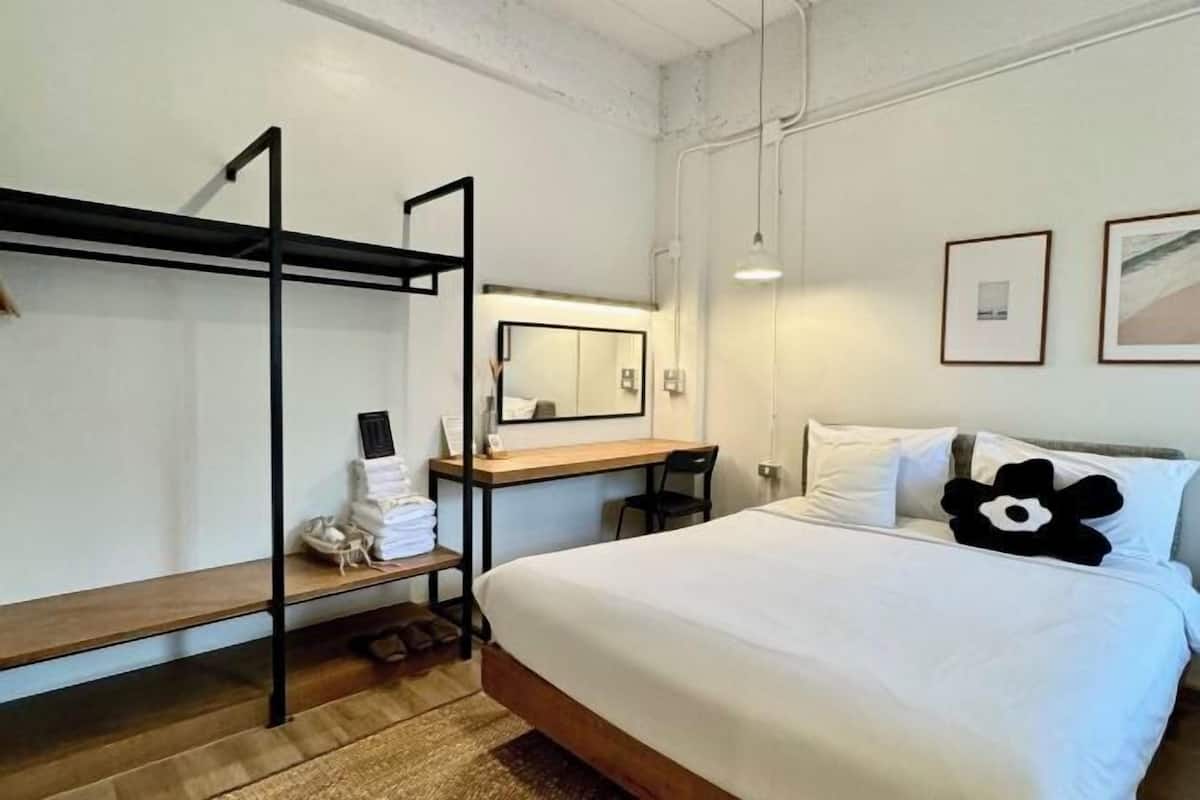 Une chambre d’hôtel avec un lit superposé, un bureau, une chaise, un lit avec une literie blanche, un miroir et deux tableaux encadrés au mur.