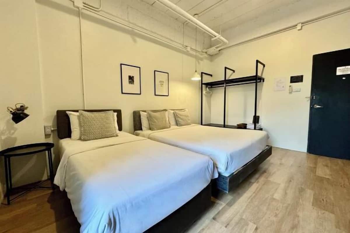 Une chambre d’hôtel avec deux lits, une petite table, un luminaire suspendu et une porte.