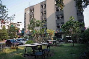 An outdoor seating area with tables and chairs, a building with balconies, and a parking lot.