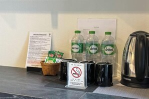 A hotel reception area with a sign, bottled water, a basket of snacks, a no-smoking sign, and a kettle.
