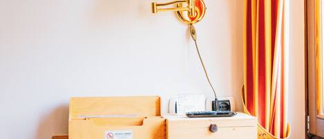 A hotel room with a wooden desk, a white lamp with a gold base, a small box, and a black device on the desk.