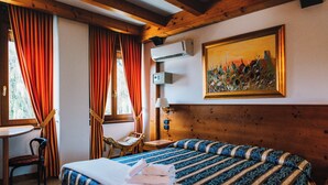 A hotel room with a wooden headboard, a bed with striped bedding, a chair, a small table, and a painting on the wall. - Arciduca Charming House (Arco)