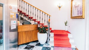 A hotel reception area with a check-in counter, a staircase with red carpeted steps, and a potted plant. - Arciduca Charming House (Arco)