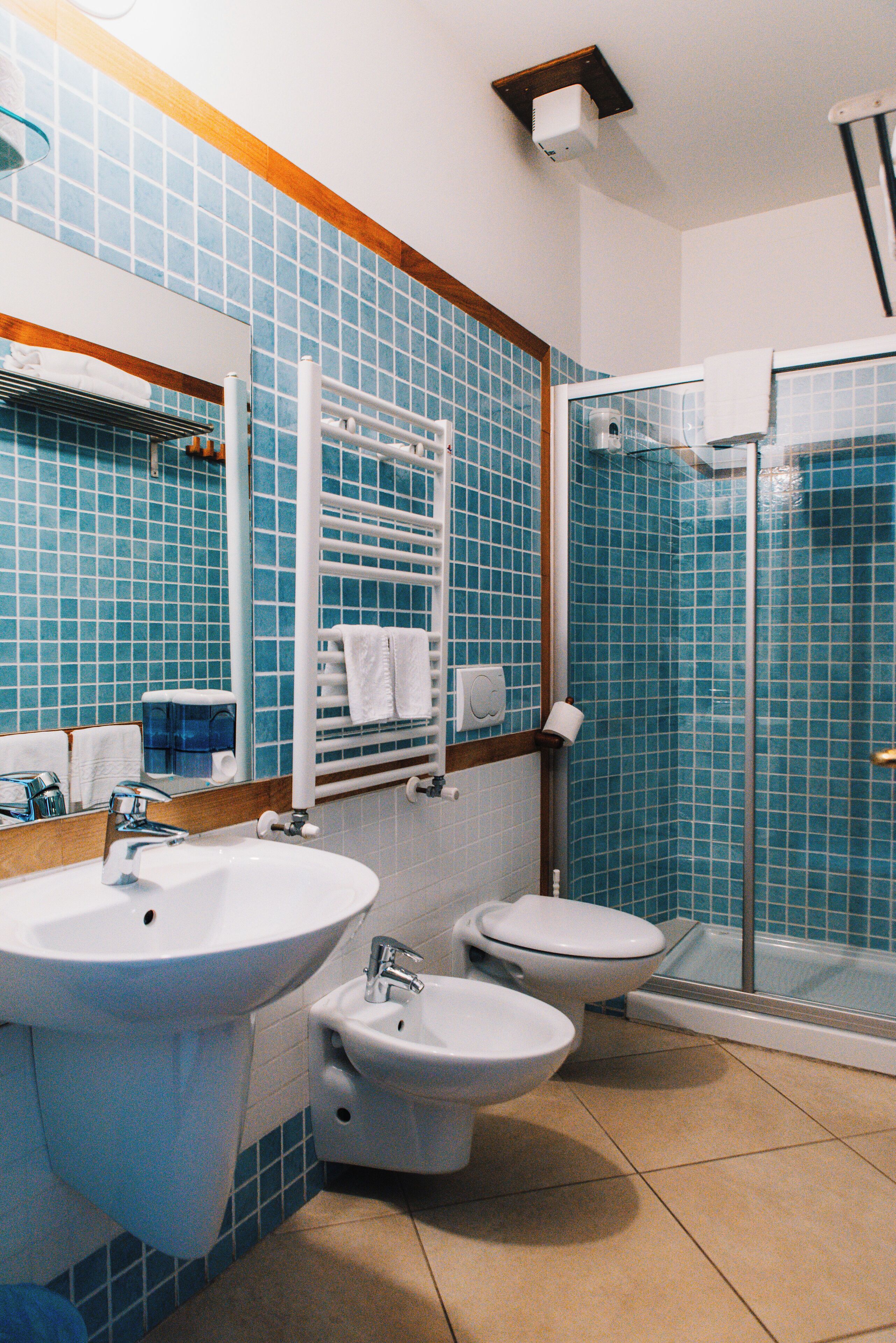 A bathroom with a sink, two toilets, a glass shower enclosure, and a towel rack.