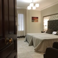 Un dormitorio con cama, mesita de noche, un cuadro y una ventana con cortinas.