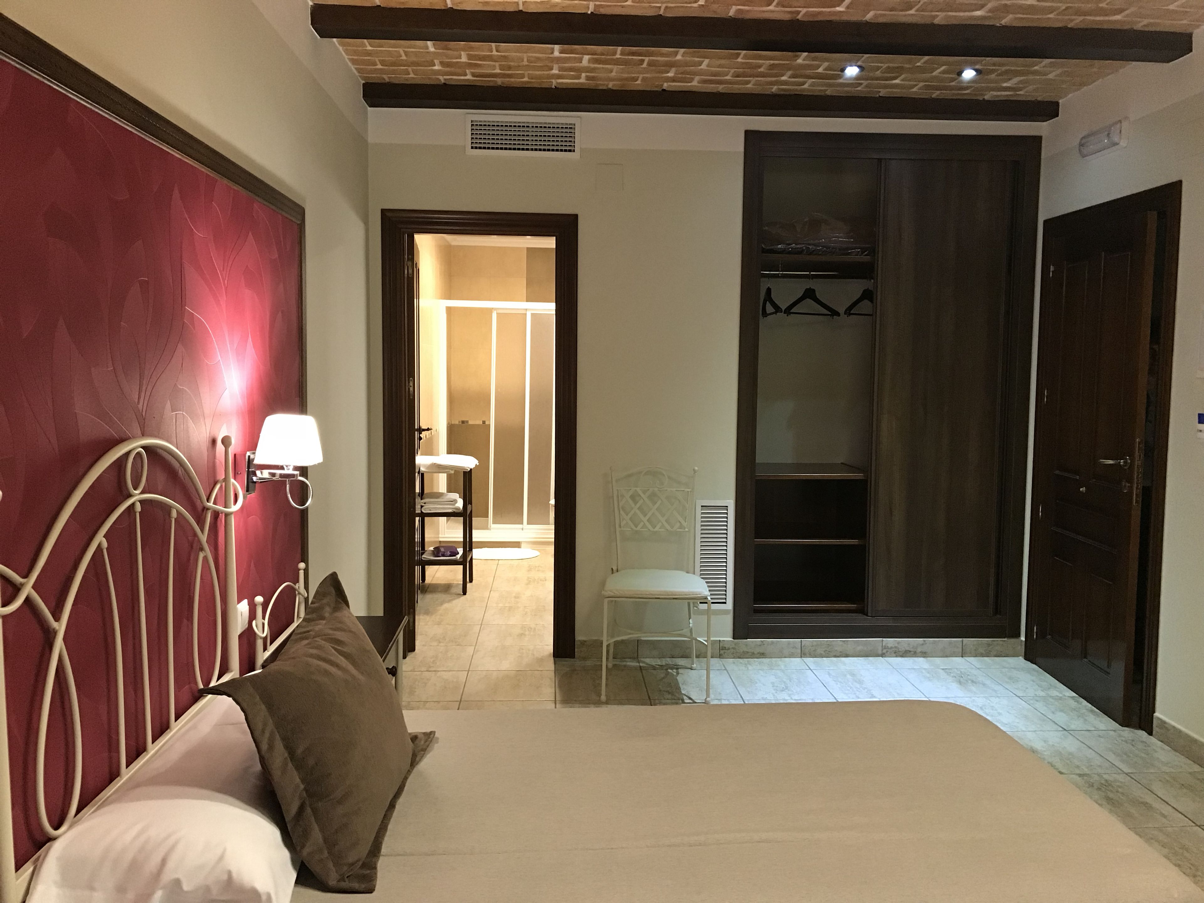 Une chambre à coucher comprenant un lit, une table de chevet, une lampe, une armoire et une salle de bain visible à travers une porte ouverte.