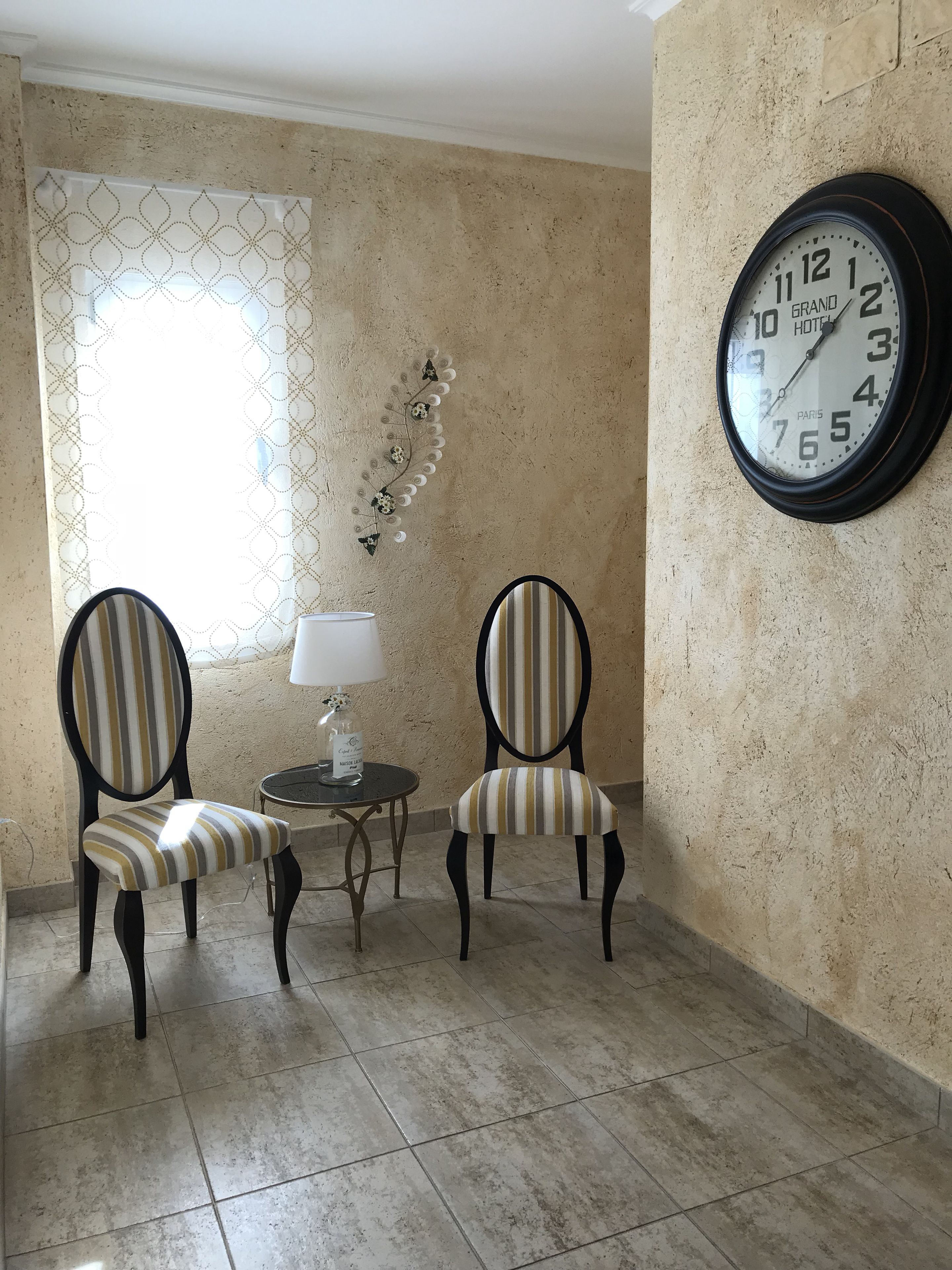 Una habitación con dos sillas a rayas, una mesita con lámpara y un reloj de pared.
