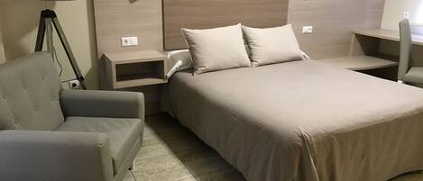 Habitación de hotel con una cama grande, una silla, una mesita de noche, una lámpara y una luz en la pared.