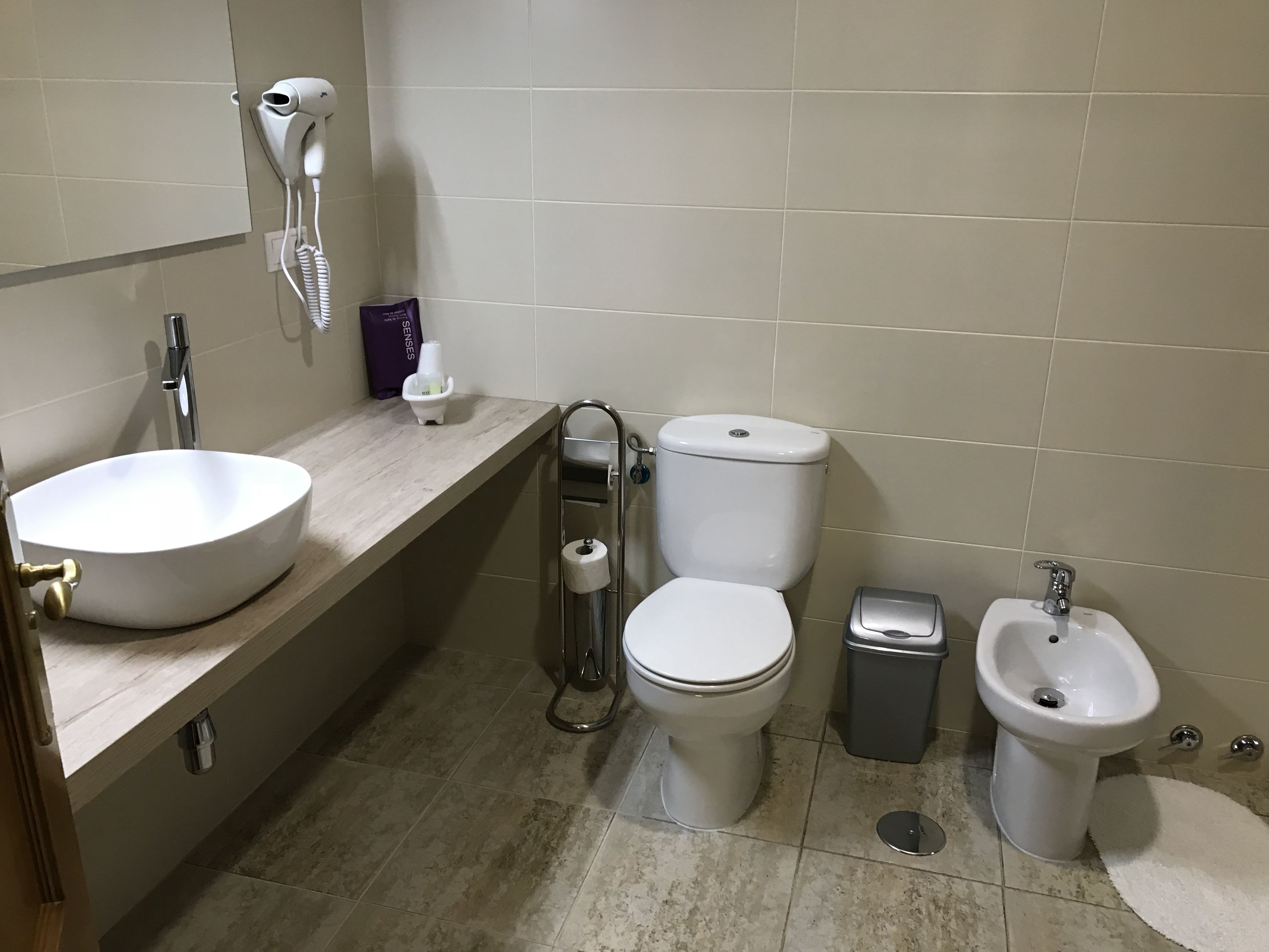 A bathroom with a sink, toilet, bidet, and a hairdryer on the wall.