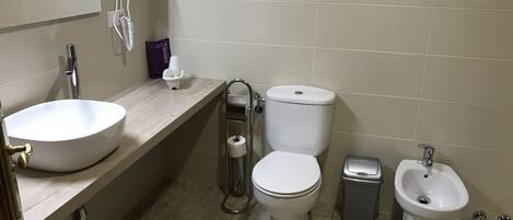 A bathroom with a sink, toilet, bidet, and a hairdryer on the wall.