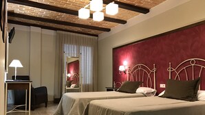 A hotel room with two beds, a desk, a chair, a mirror, and a red accent wall.