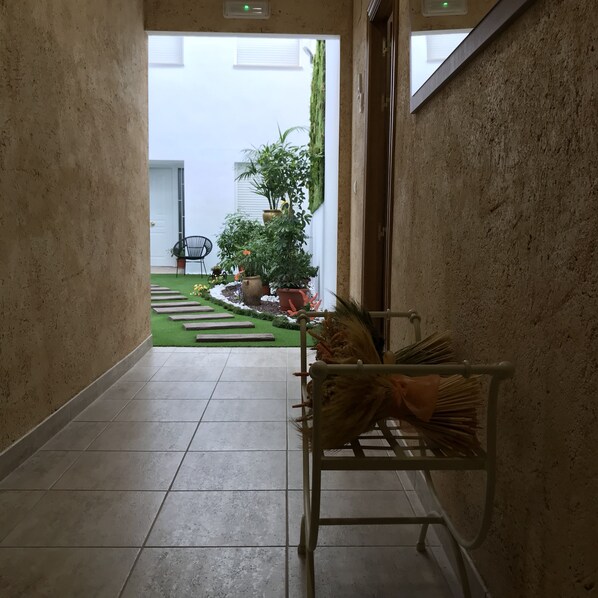 A corridor with tiled flooring leading to a garden area with potted plants and a chair.