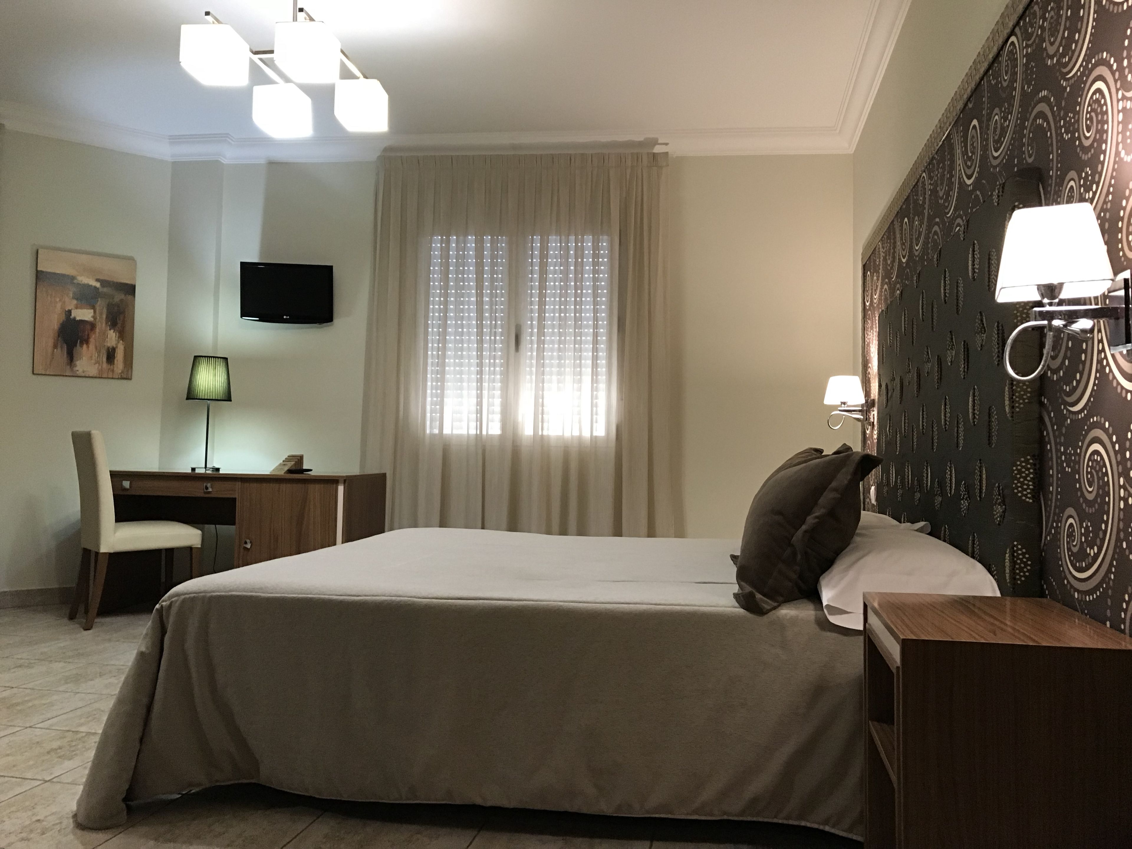 A hotel room with a bed, a desk, a chair, a TV, and a window with curtains.