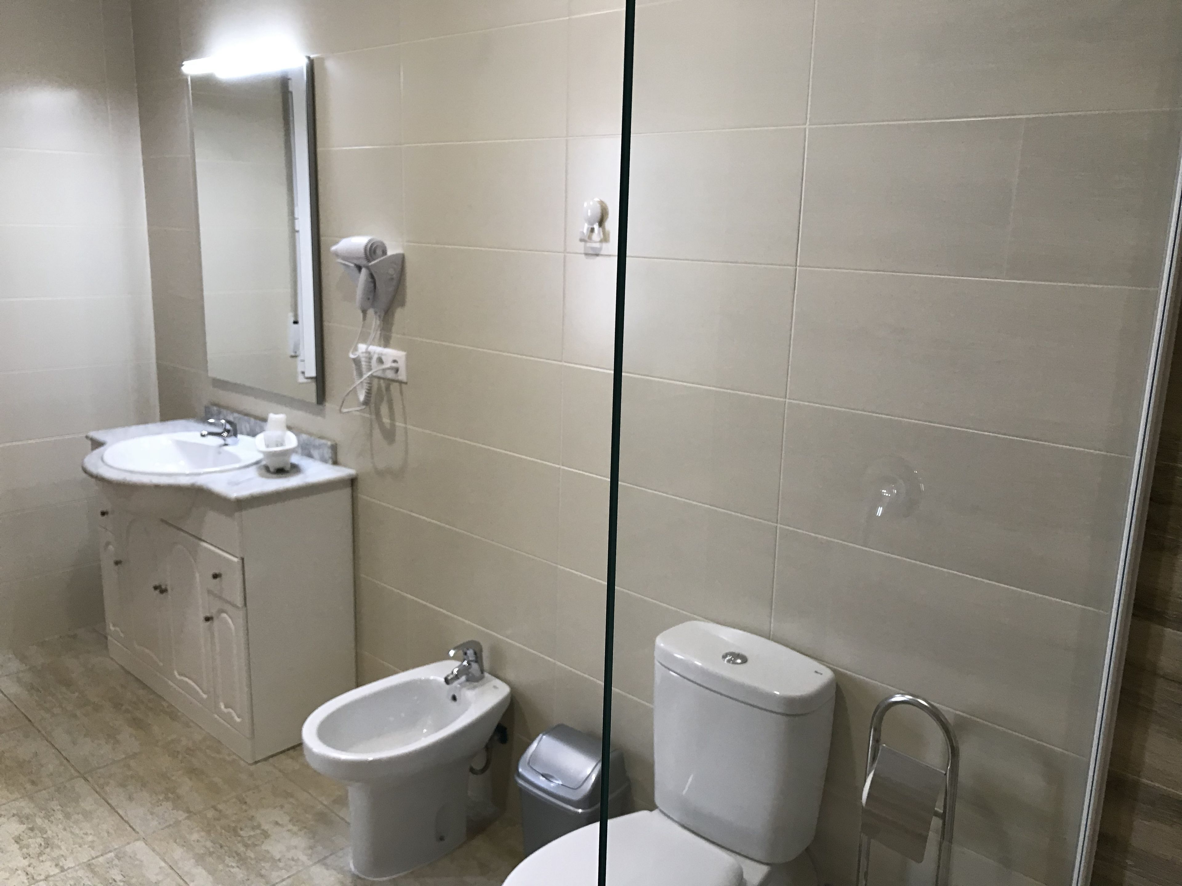 A modern bathroom with a sink, bidet, toilet, and glass shower enclosure.