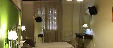 A room with two beds, a desk with a computer, a chair, a TV, and a window with curtains.