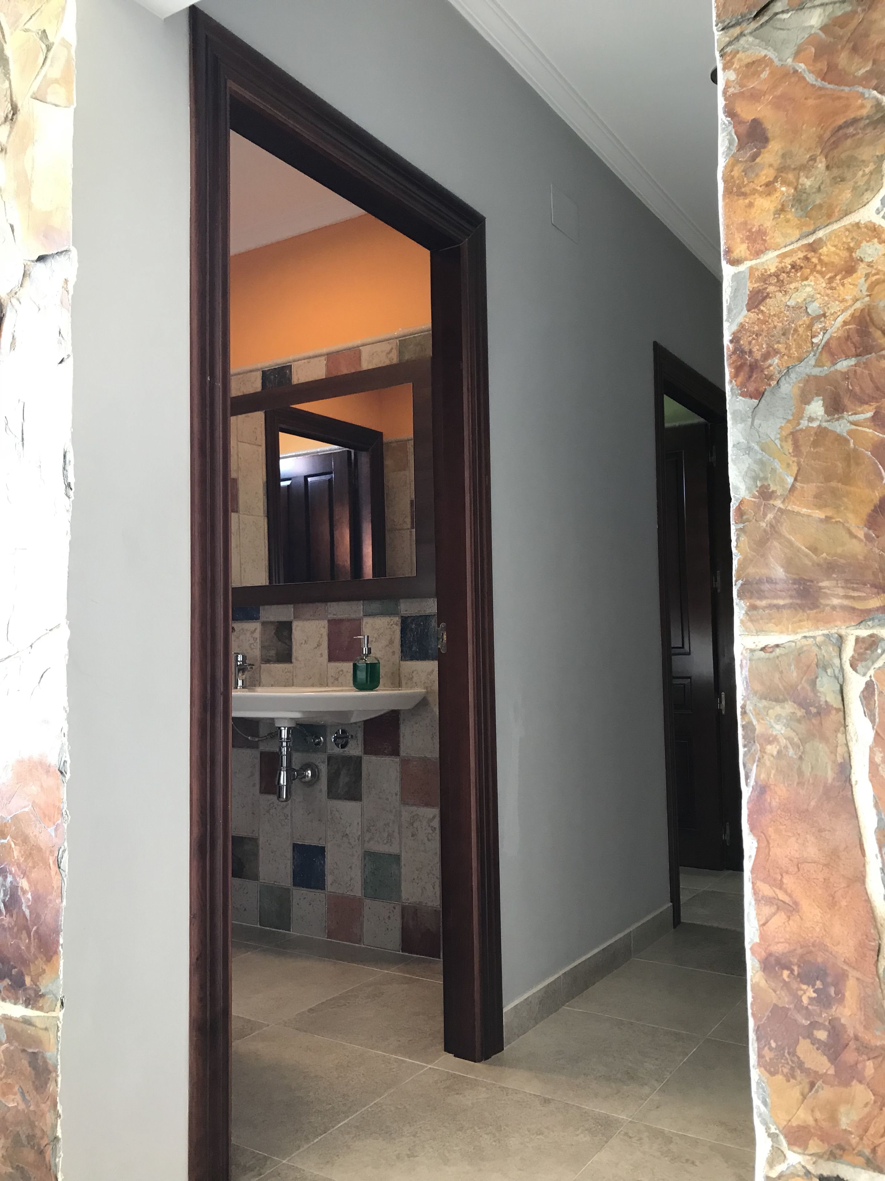 Un pasillo que conduce a un baño con suelo de baldosas, un lavamanos y un espejo.