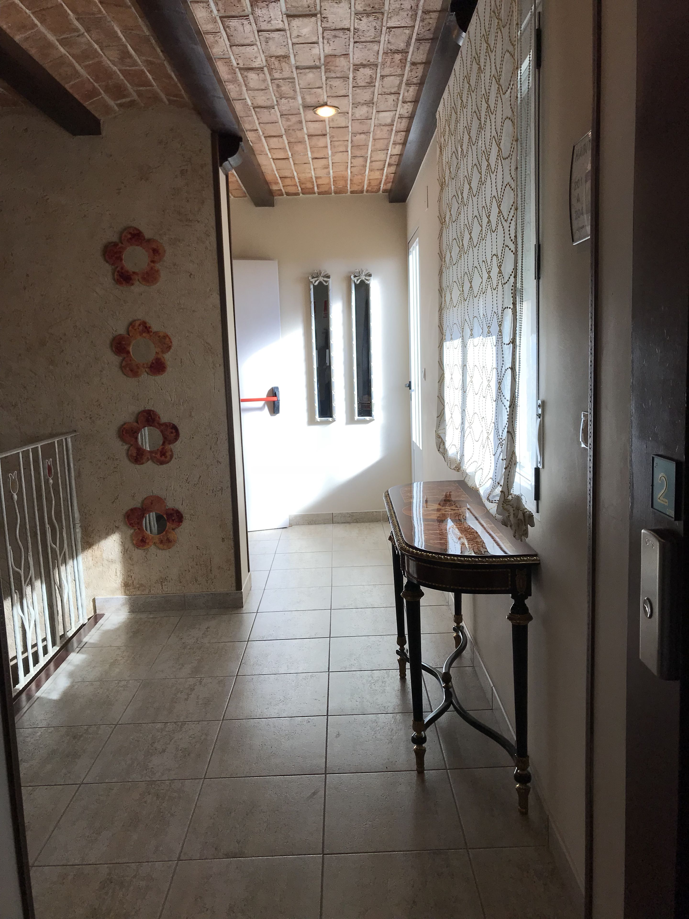 A hallway with a tiled floor, a wooden table, and a door with a red handle.
