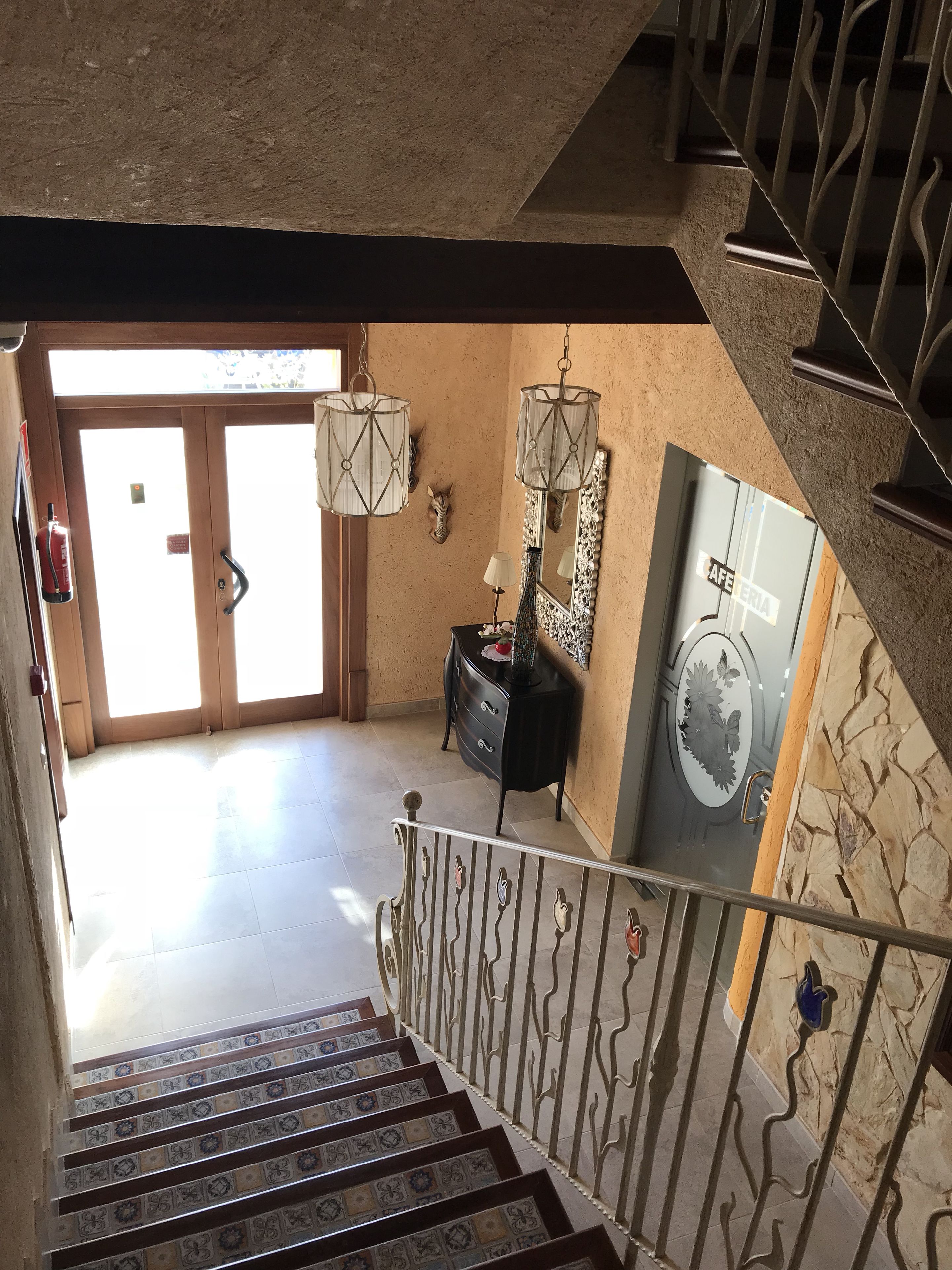 A staircase with patterned tiles leading to a room with a large mirror, a dresser, and a door with a fire extinguisher.