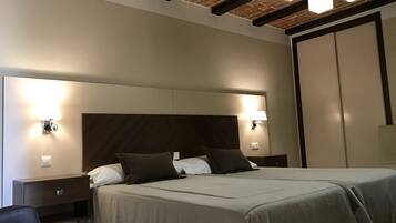 Habitación de hotel con una cama grande, dos mesitas de noche, un armario y un techo con ladrillo visto e iluminación empotrada.