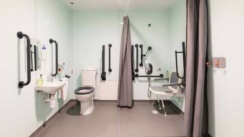 A modern bathroom with a toilet, sink, shower, and grab bars.