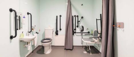 Un baño moderno con inodoro, lavabo, ducha y barras de apoyo.