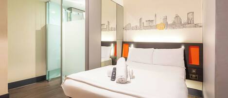 A hotel room with a bed, a remote control, a towel, a nightstand, and a cityscape mural on the wall.