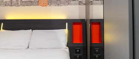 A hotel room with a bed, a cityscape wall art, and a modern headboard with red accents.