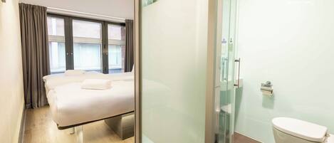 A modern hotel room with a bed, a glass shower enclosure, and a toilet.