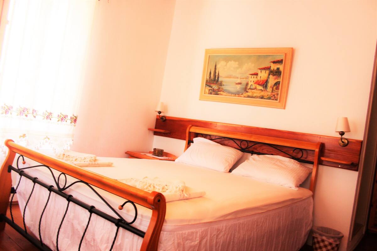 A neatly made bed with a wooden headboard, a bedside table with a lamp, and a painting on the wall.
