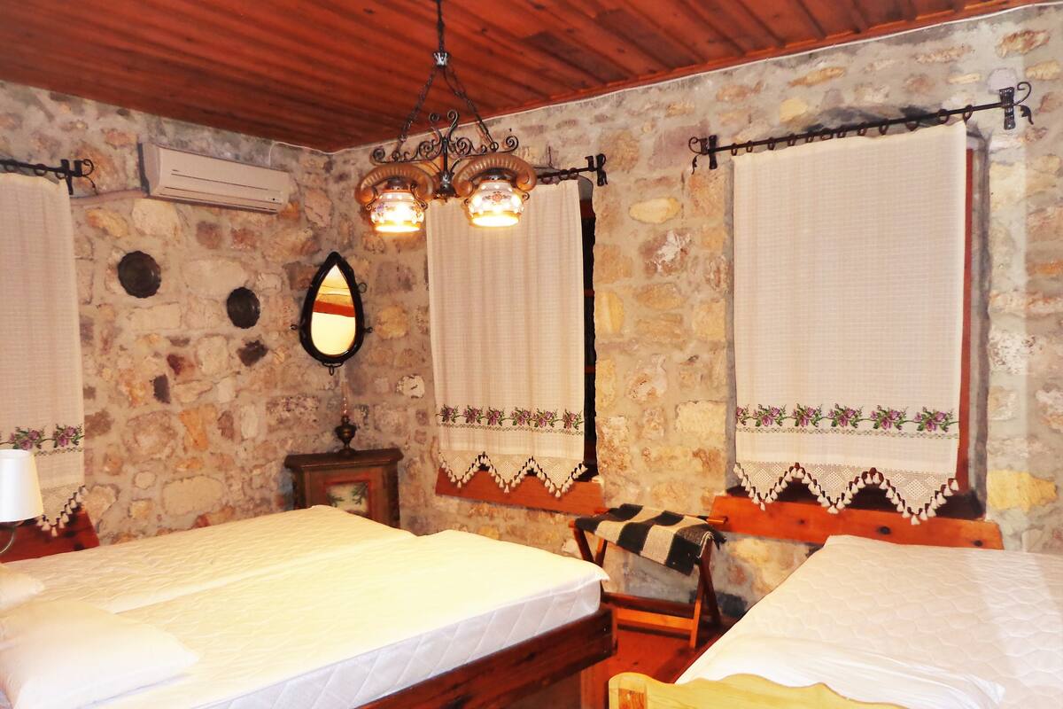 A room with two wooden beds, stone walls, a mirror, and a chandelier.