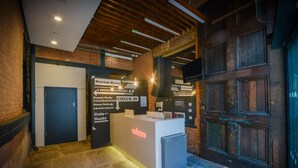 A reception area with a check-in counter, directional signs, and a wooden door. - easyHotel Manchester (Manchester)