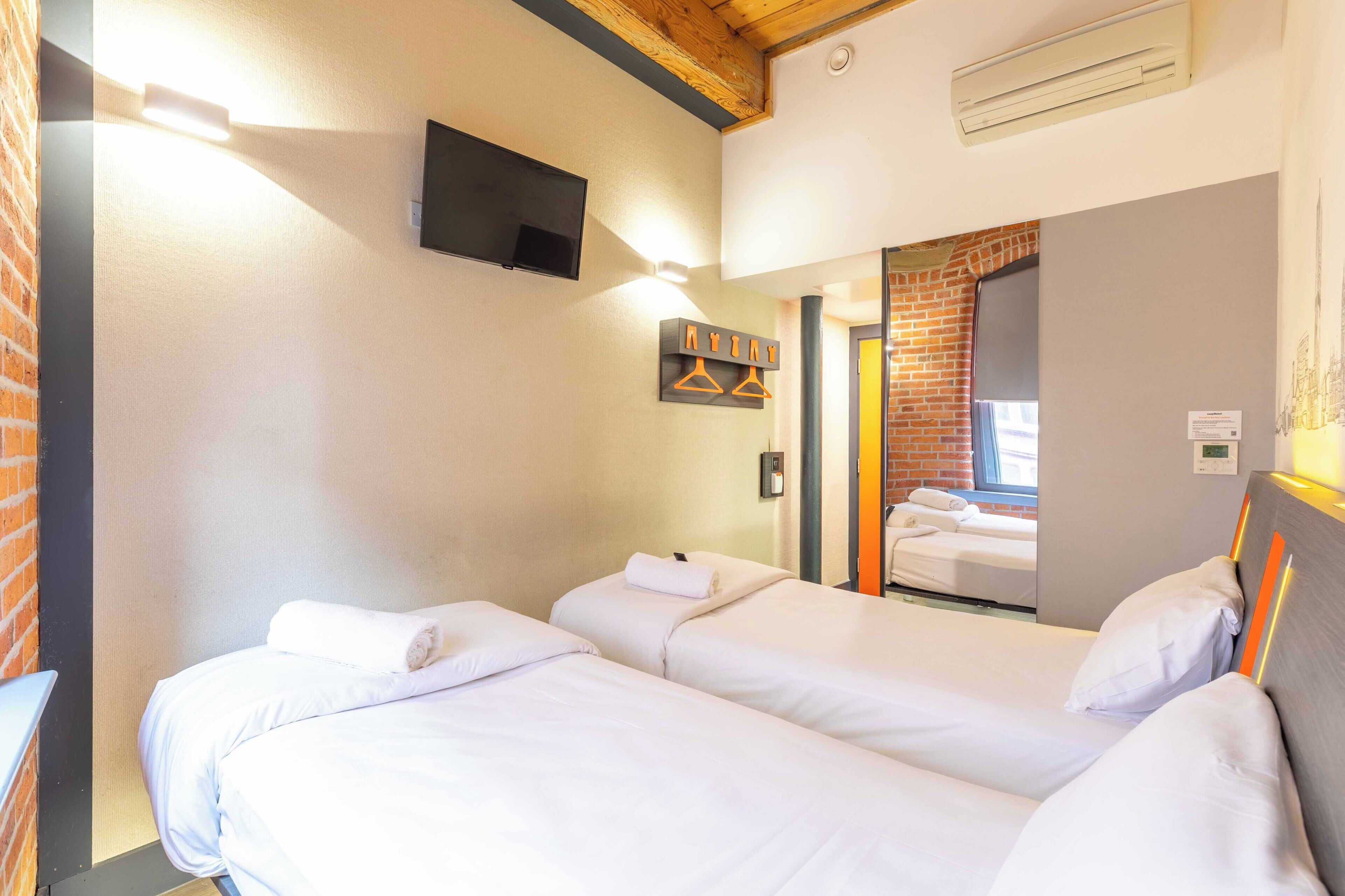 Habitación de hotel con dos camas, un televisor de pantalla plana montado en la pared y una pared de ladrillo.