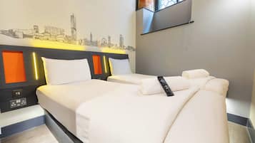 A hotel room with two beds, a cityscape wall art, a TV mounted on the wall, and a window with a view.