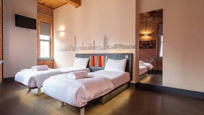 A hotel room with two beds, a cityscape mural, a TV, and a brick wall. - easyHotel Manchester (Manchester)