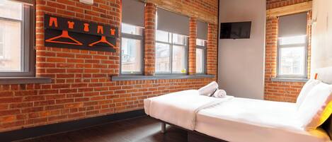 A room with a brick wall, wooden beams, a bed, a TV, and a window with a view.